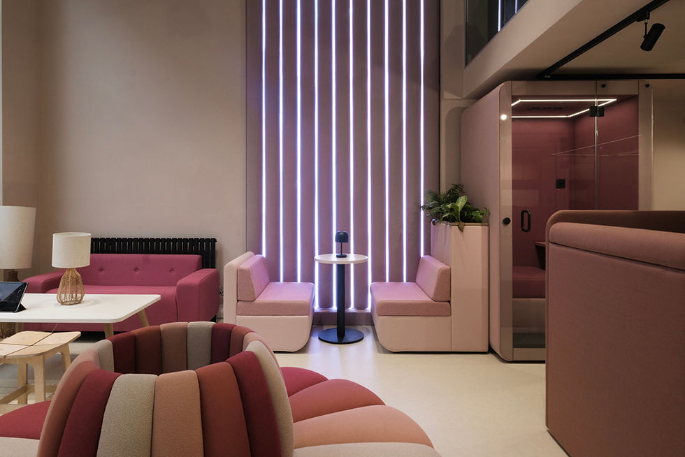 Modern lounge with pink and maroon seating, a small table, and a lamp. Vertical LED lights on wall, sleek and calming atmosphere.
