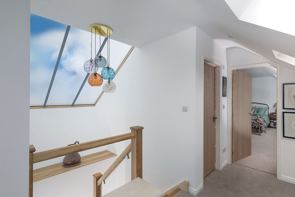Stairwell with colorful glass pendant lights, skylight showing blue sky, open door to a bedroom with floral bedding, light wood accents.