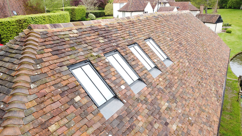 A tiled cottage roof with four skylights, set in a green countryside estate beside a pond.