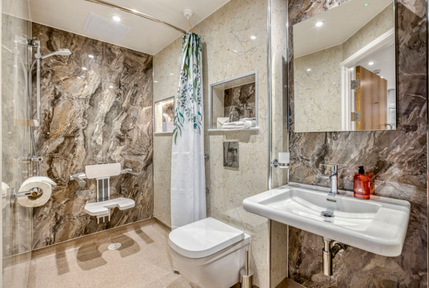 Modern marble bathroom with glass shower, wall-mounted sink, toilet, and floral shower curtain in a bright, tidy space.