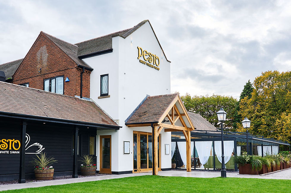 Exterior of Pesto Great Italian Food restaurant, a white and brick building with patio, lamps, and green lawn under cloudy sky