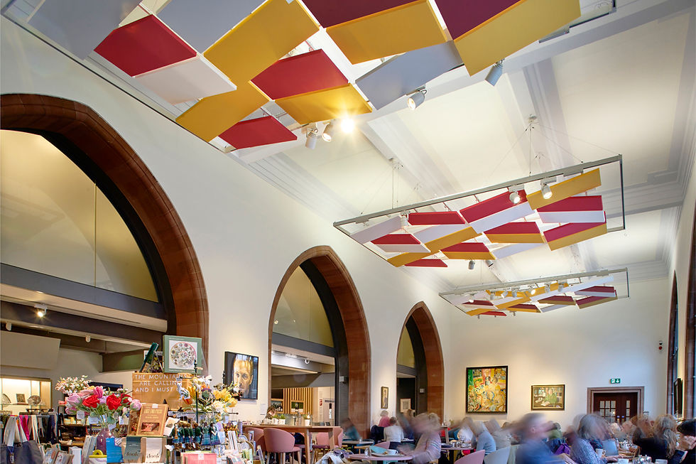 Interior of a cafe with arched windows, colorful ceiling panels, and blurred people at tables. Bright flowers and art add a lively vibe.