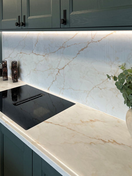 Modern kitchen with marble countertop and backsplash, black stovetop, and potted plant. Dark green cabinets and ambient lighting.