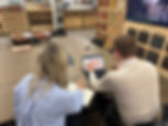 Two coworkers review flooring samples on a laptop in a showroom, with sample racks and wood swatches around them.