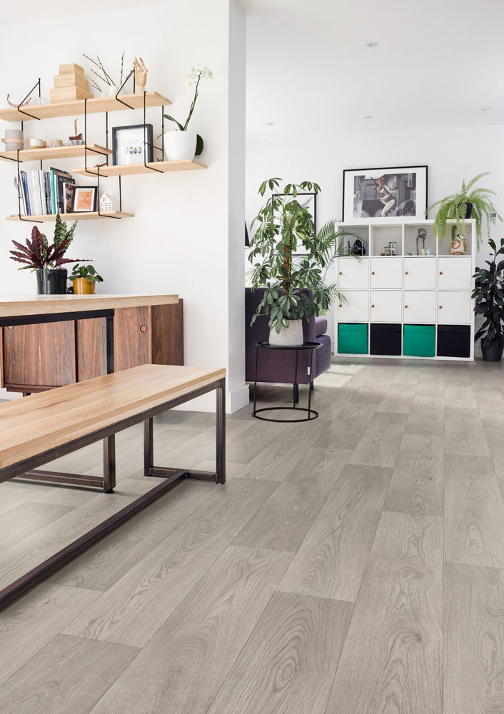 Modern living room with wooden shelves, plants, a white and green cabinet, and gray wood flooring. Bright and tidy space.