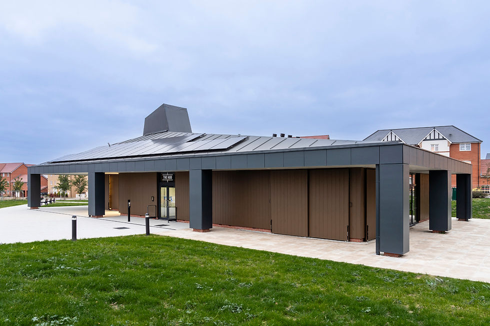 Modern building labeled "The Hub" with dark exterior, solar panels on the roof, surrounded by grass and other houses under a cloudy sky.