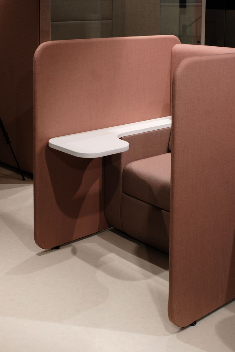 Brown upholstered office pod with a cushioned seat and a white desk, set on a beige floor. The design is modern and minimalist.