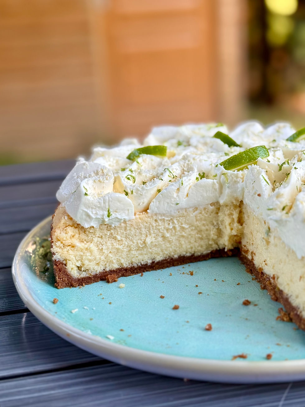 Part de key lime pie sur assiette bleue, avec une part entamée, en lumière douce sur table extérieure.