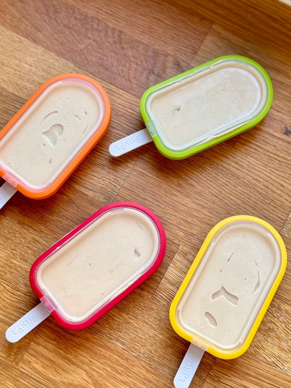 Quatre glaces en bâton dans des moules orange, vert, rose et jaune sur un parquet, marque Lekué visible. Bâtonnets glacés spéculoos (façon Magnum)