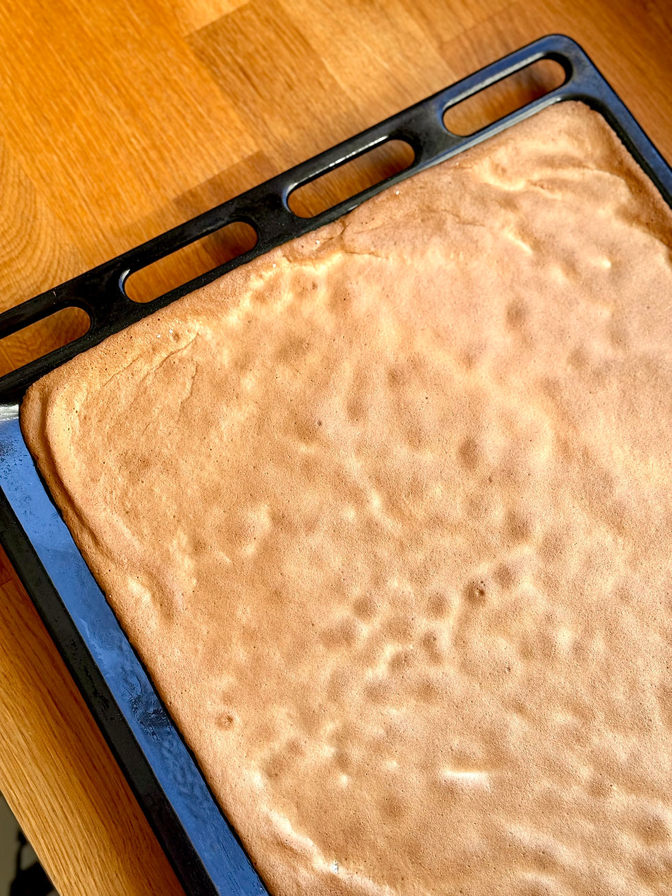 Pâte à biscuit pain de gênes dorée sur plaque de cuisson noire, reposant sur un comptoir en bois clair. Ambiance chaleureuse et appétissante.