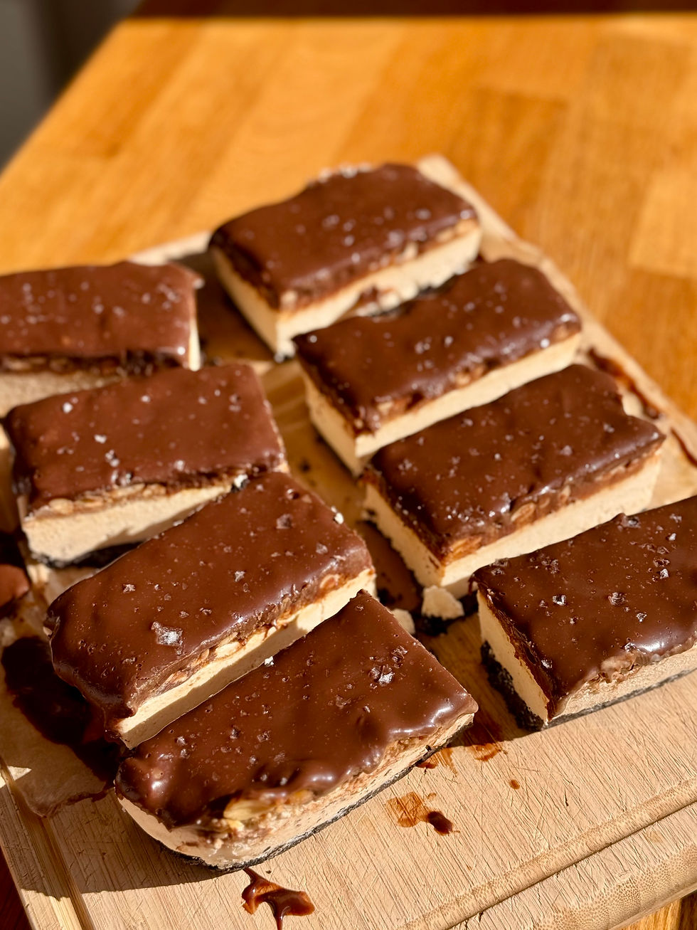 Barres glacées Snickers parsemées de sel, empilées sur une planche en bois, sous une lumière chaude.