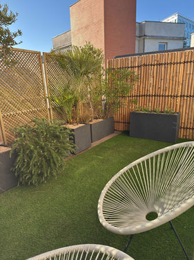 Terrasse aménagée à Saint-Ouen : gazon, fauteuils, brise-vue bambou et jardinières anthracite