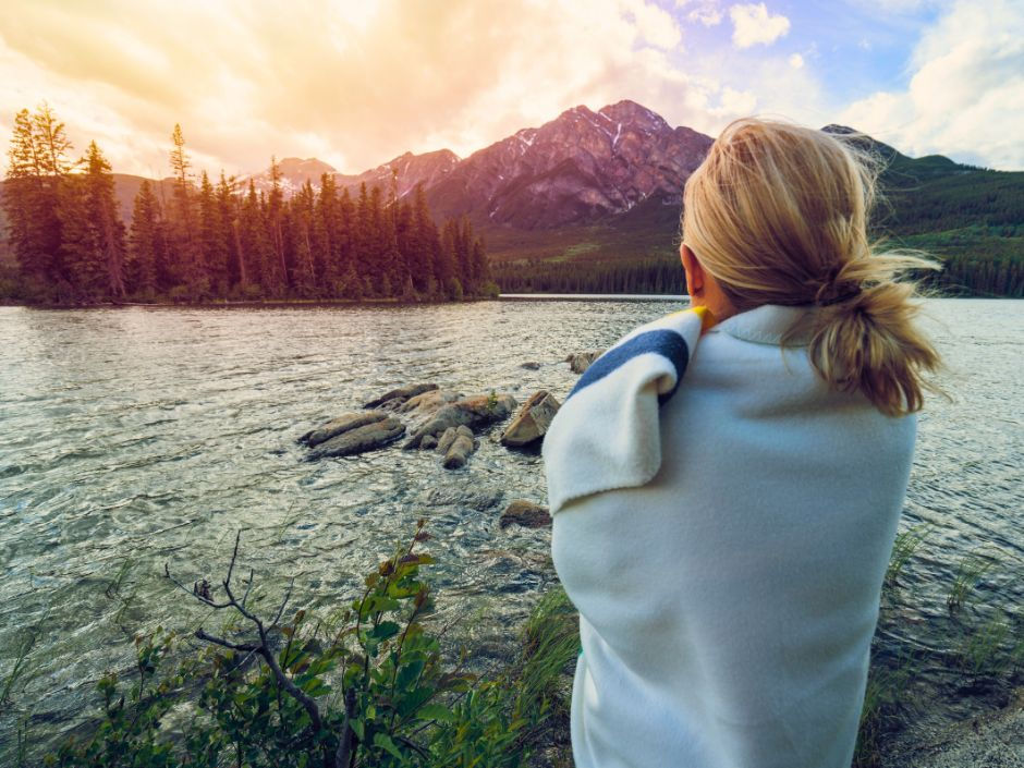 Woman standing by a lake at sunrise, facing the water