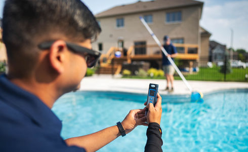 Man checks pool's pH with phone near pool; another cleans it. Mississauga pool service