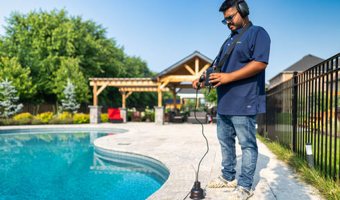 Man inspecting underground pool with plumbing with a leak detection equipment near a pool with trees PoolZenia pool leak detection service