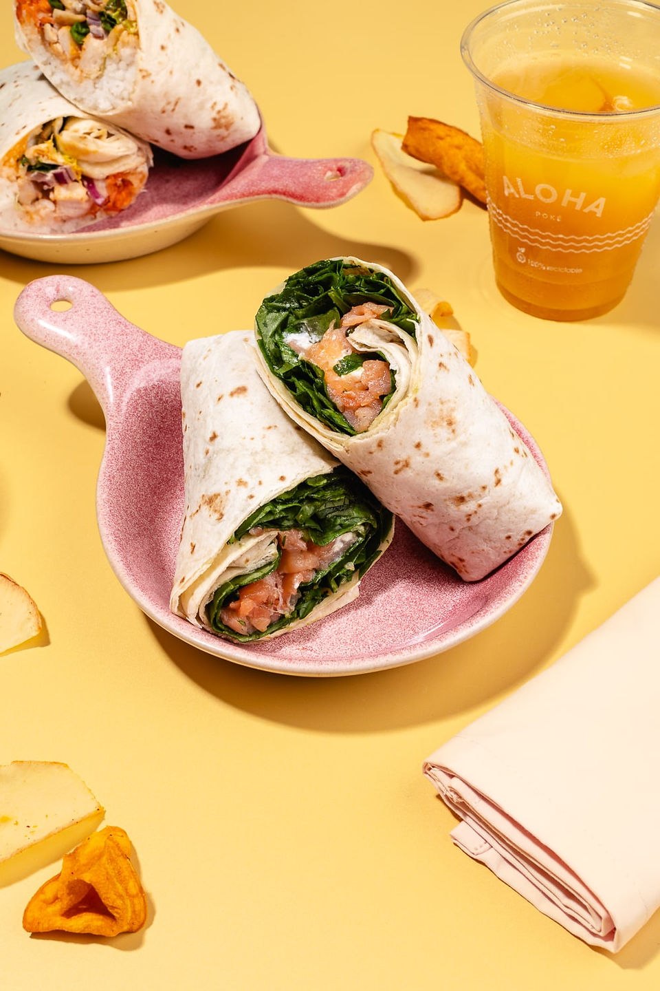 Primer plano de wraps rellenos servidos en plato rosa, acompañados de bebida fresca sobre fondo amarillo.