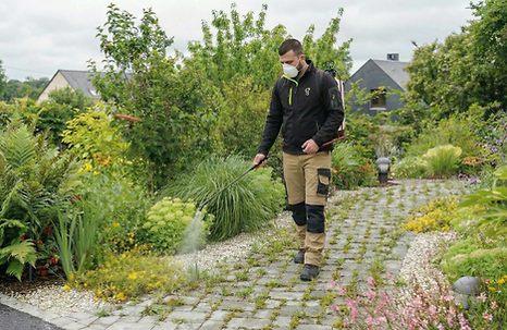 Photo d'un employé de Gaïa Jardin en train de pulvériser du produit sur des dalles entourées d'herbe. L'employé porte un masque de protection.