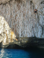 Climber scaling cliff inside sea cave with turquoise water below in Paxos Island