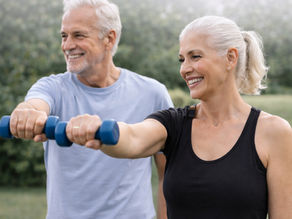 Casal de idosos praticando exercício físico ao ar livre, realizando treino de força com halteres, representando envelhecimento ativo, saúde funcional, autonomia e longevidade com qualidade de vida.