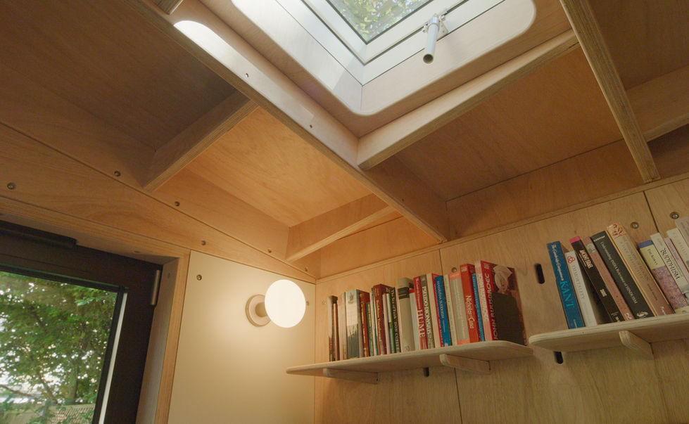 Interior view of skylight window and bookshelf inside bespoke London garden room with plywood ceiling.