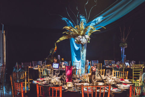 The interior of a carnival themed party marquee. A dark, starlit marquee drape in the background with an elaborate tall table centre piece in the foreground