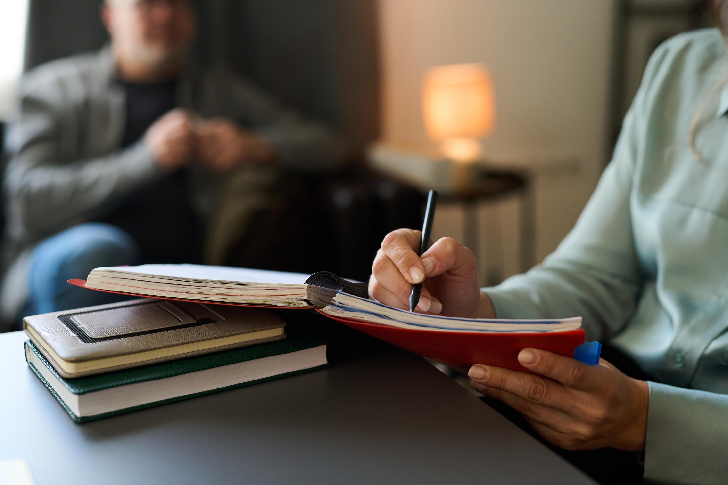 A coach taking notes in a notebook during a conversation, with a warm lamp behind