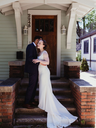 Nancy and Ammar share a sweet, private moment on the steps of a craftsman-style home, with Nancy smiling as she leans into Ammar. Her elegant gown cascades down the brick steps.