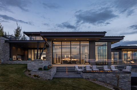 Modern home exterior at dusk, showcasing expansive glass walls and stonework