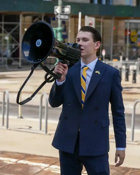 A man in a suit speaking through a megaphone on a city street