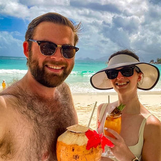 Two people stand on a tropical beach in the Seychelles with cocktails in hand