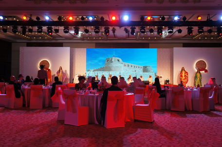 Audience seated in an event, screens displaying the event name and details
