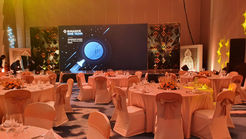Round tables set for a formal corporate gala dinner with stage in the background.