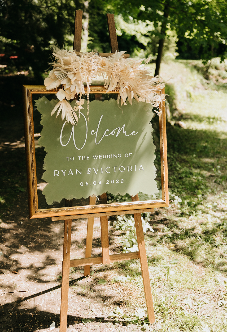 Wedding reception sign with a sage green background and white text that reads 'welcome to the wedding of Ryan and Victoria'