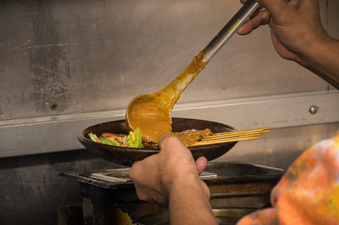 Freshly grilled chicken sate being coated with house-made peanut sauce in North London