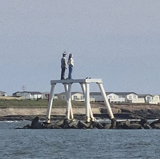 Women visiting The Couple (Ebb & Flo) bronze sculpture in Amble, Northumberland, coastal breakwater art installation overlooking the sea.