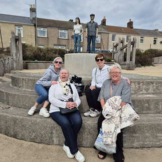 Women visiting The Couple (Ebb & Flo) bronze sculpture in Amble, Northumberland, coastal breakwater art installation overlooking the sea.