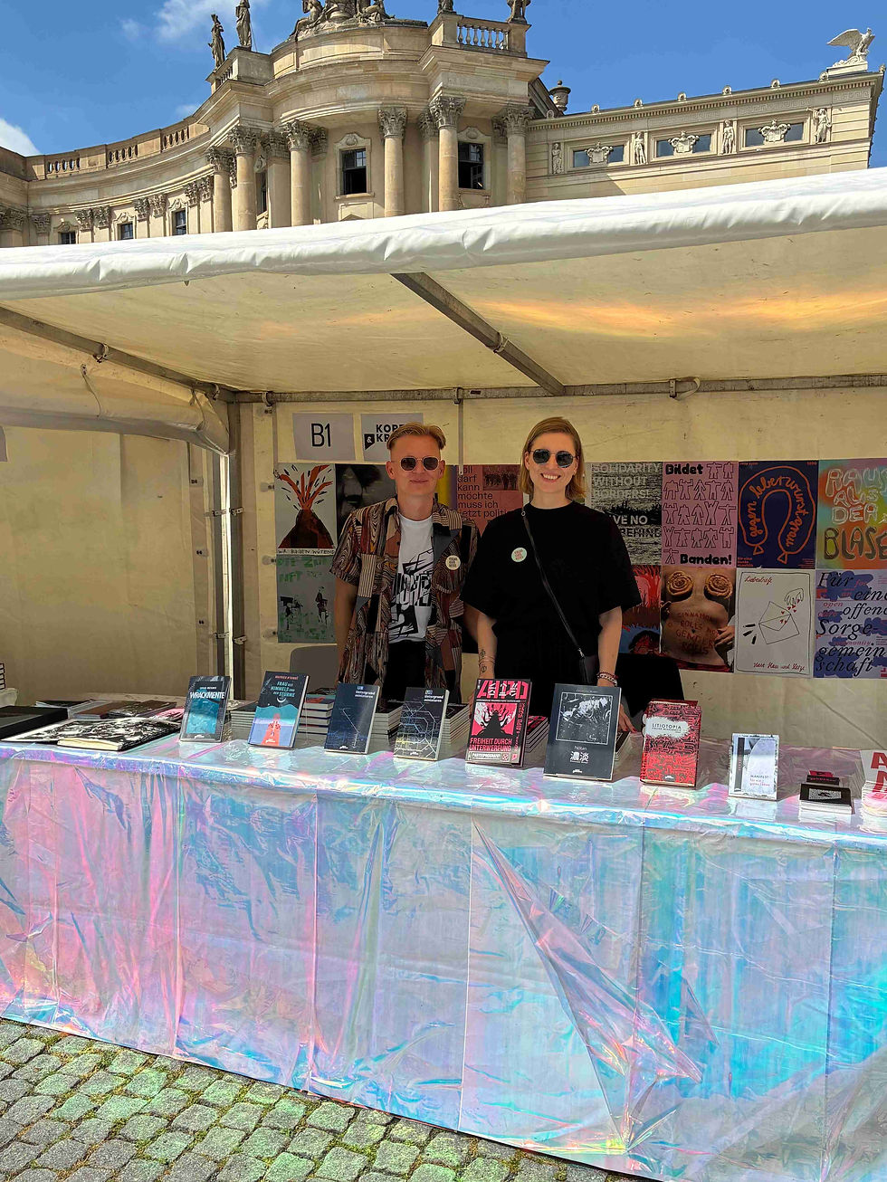 Des Verleger des Kopf & Kragen Verlags steht mit Paulina Kasprzyk in einem Stand auf dem Berliner Bücherfest am Bebelplatz. Im futuristisch dekorierten Stand sin die Bücher des Verlages zu sehen und die Plakatausstellung des Aktionsbündnisses Verlage gegen Rechts