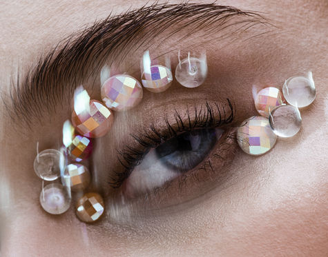 Close-up view of a model’s eye with dramatic makeup, rhinestones, motion blur and creative lighting