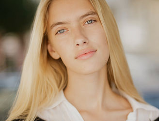 Ein professionelles Headshot-Porträt einer jungen, blonden Frau. Sie blickt freundlich und selbstbewusst in die Kamera
