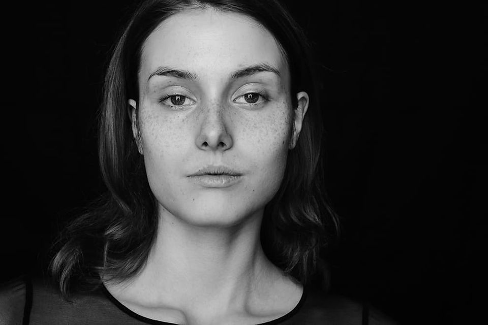 Monochromatic portrait of a woman with freckles, expressing serenity against a dark background.