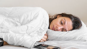 A women lying on her side in bed, side-eyeing her cell phone.