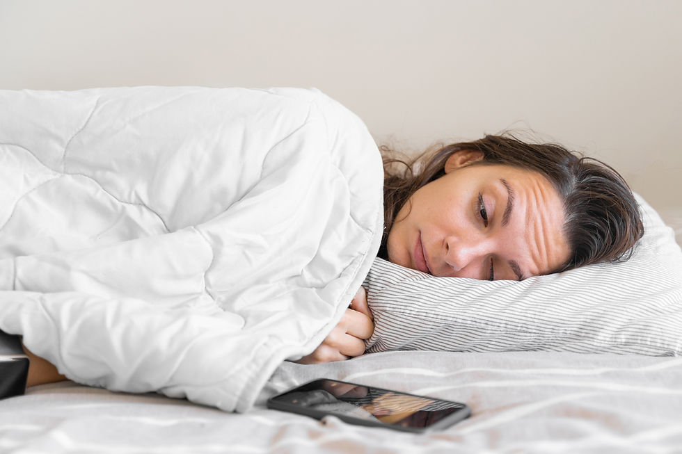 A women lying on her side in bed, side-eyeing her cell phone.