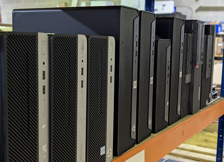 Multiple black and silver desktop computers lined up on an orange shelf.