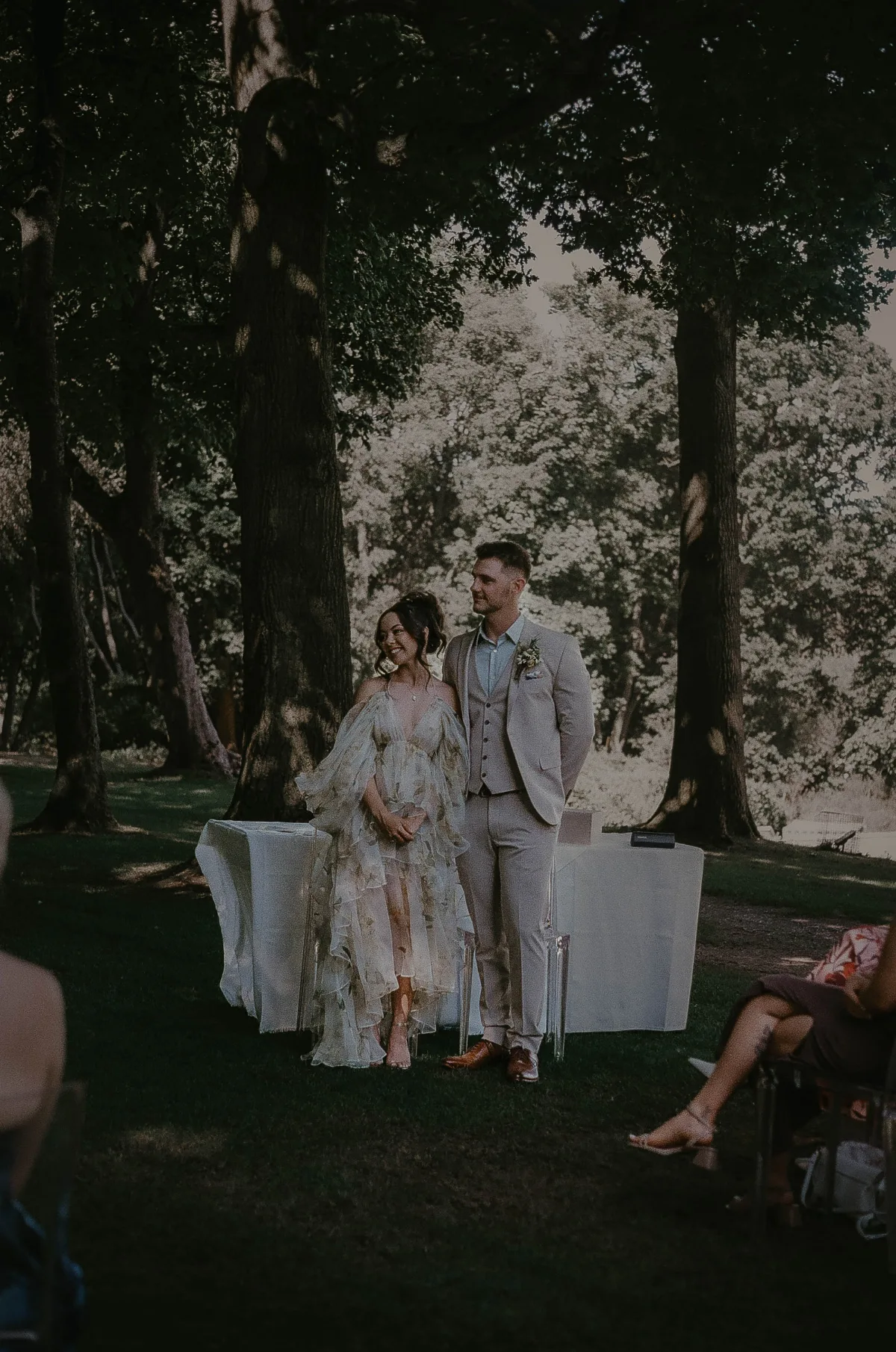A bride and groom stand together at their wedding ceremony, smiling at someone off camera. 35mm film wedding photography in Suffolk by Mikaela Jade.