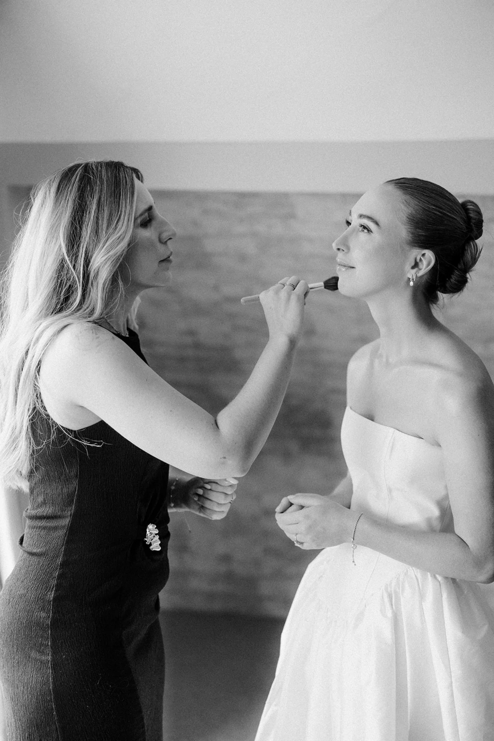 Wedding makeup artist Emily Chantal applies makeup with a brush to a bride's collarbones.