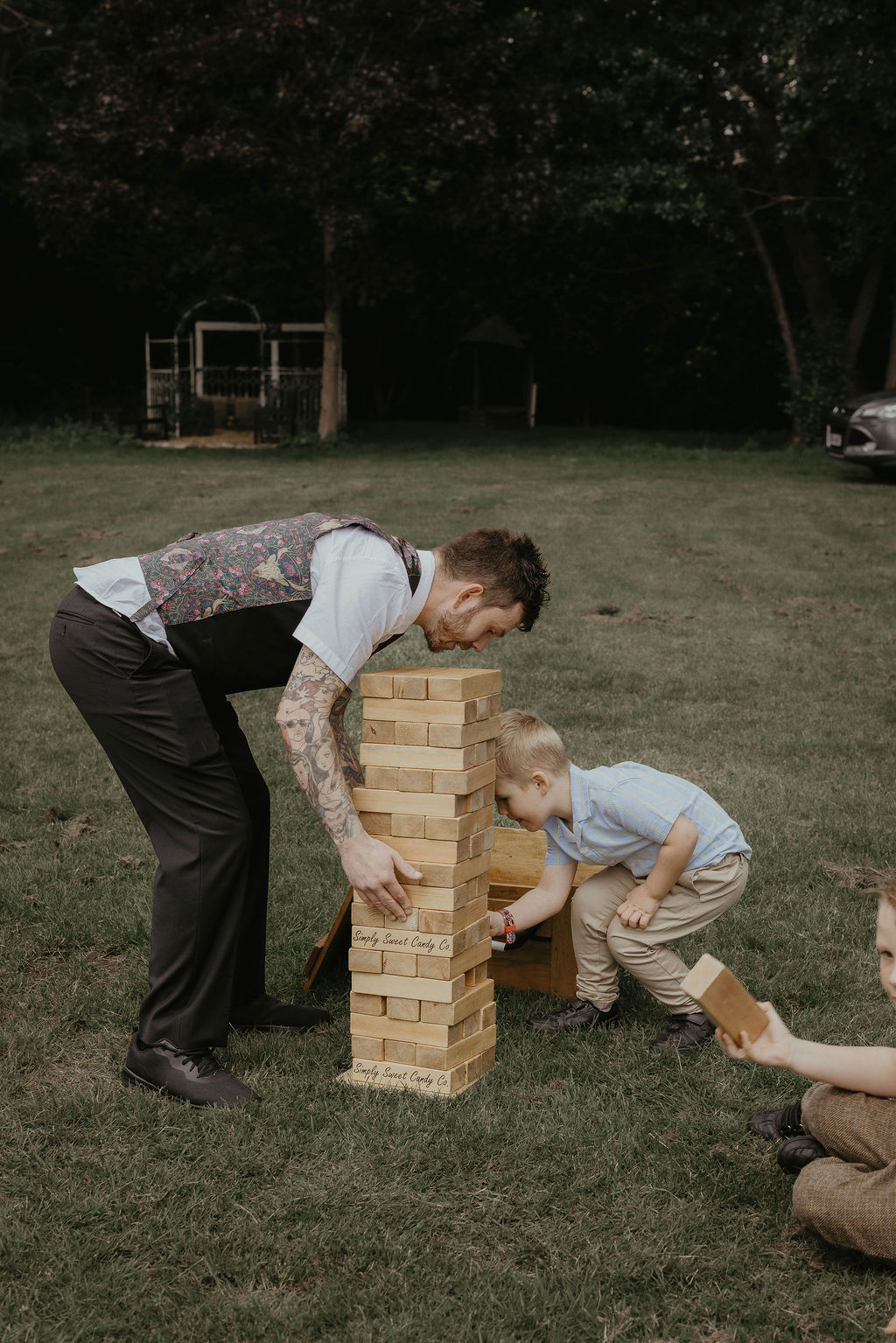 A man and a child play giant jenga on a lawn at a wedding. By Suffolk wedding photographer Mikaela Jade.