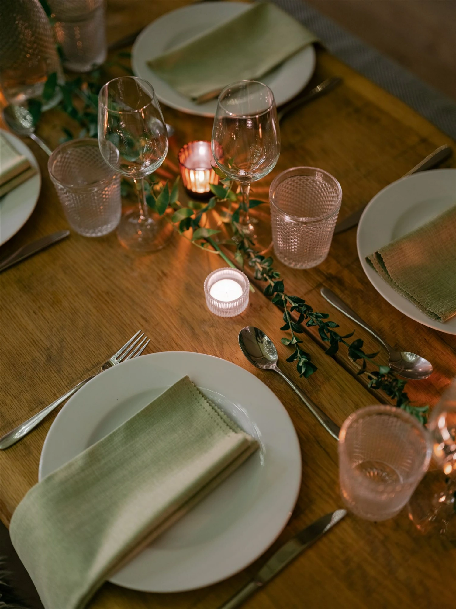 A view of a table set with candles, crockery and green napkins.