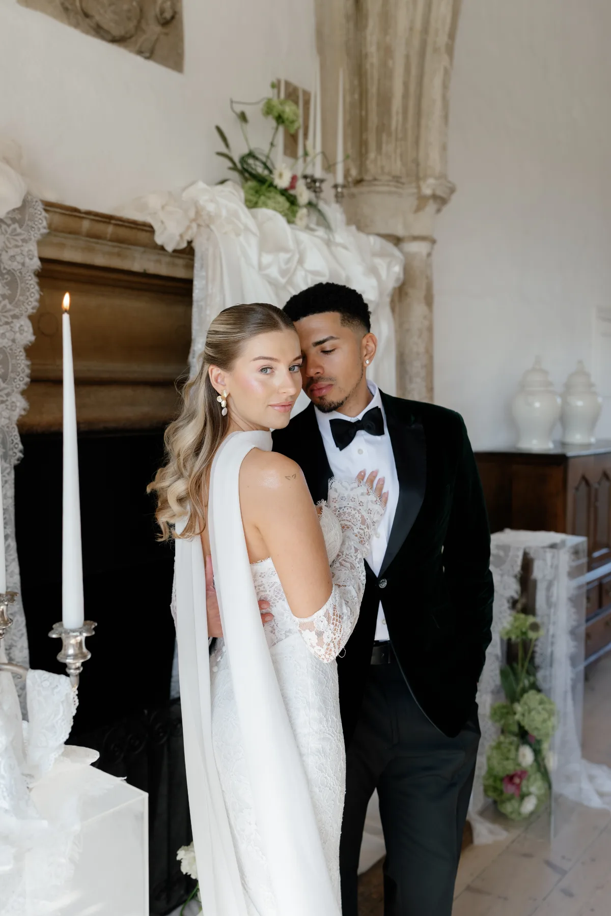 A bride looks over her shoulder at the camera while posing with her husband, wearing makeup by Suffolk makeup artist Emily Chantal.