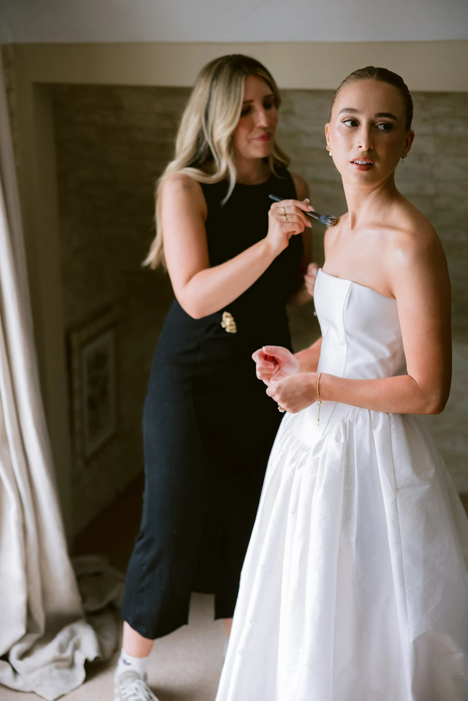 Wedding makeup artist Emily Chantal applies makeup with a brush to a bride's collarbones.