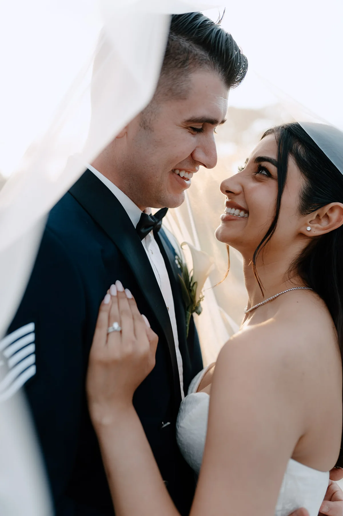 A bride, with makeup by Suffolk makeup artist Emily Chantal, smiles at her groom, surrounded by a white veil.